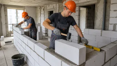Двоє будівельників у помаранчевих касках укладають блоки з газобетону під час зведення стін у приміщенні