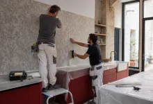 Двоє майстрів акуратно клеять шпалери з рослинним візерунком на стіну під час ремонту кухні